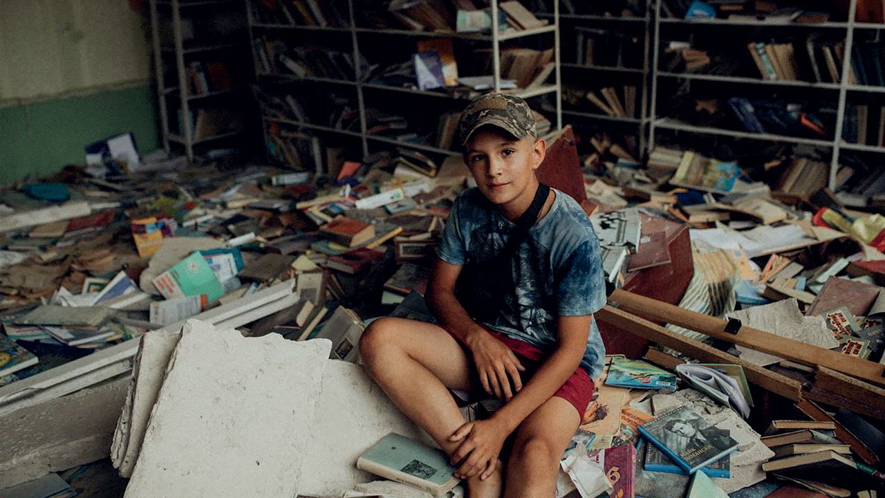En pojke sitter bland förstörda böcker
